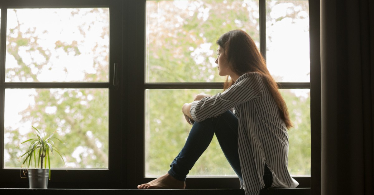 A sad millennial sitting on a window sill, millennials are dissatisfied with their personal relationships